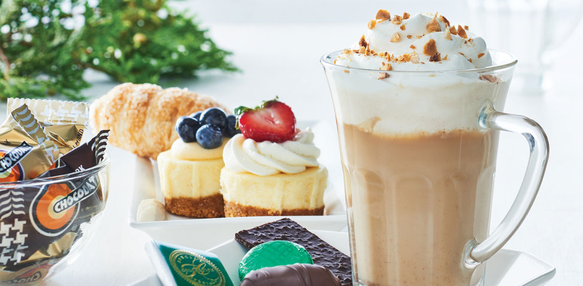 Clear tall mugs of spiced hazelnut latte next to a plate of holiday treats.