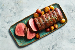 Top-down view of table with serving dish of beef wellington with roasted potatoes on a green platter.