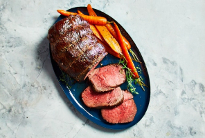 Top-down view of roast sirloin and slices of roast sirloin on dark blue serving dish with side of roasted carrots.