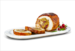 Stuffed, fresh turkey breast filled with pork, cranberry, and apple stuffing on a white serving platter with the first slice carved off.