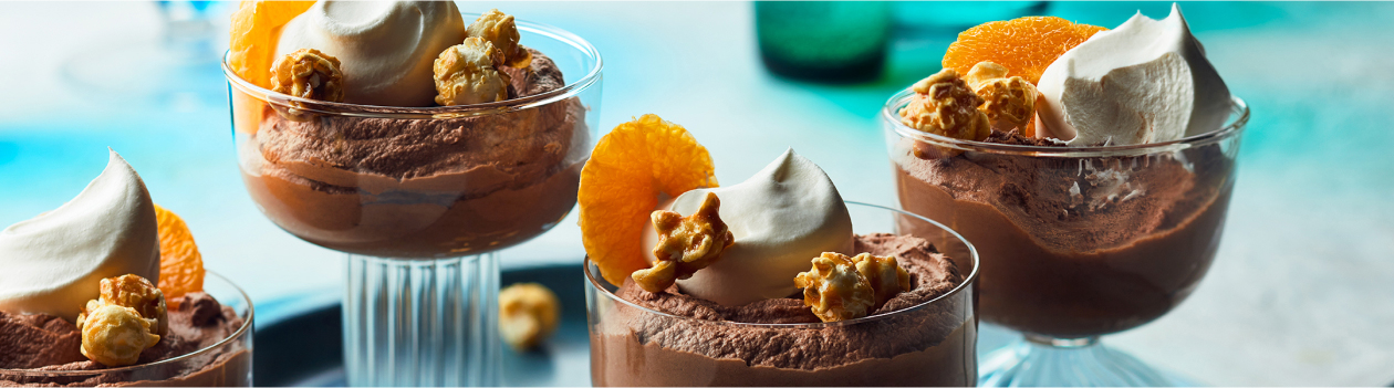 clear glass cups with chocolate mousse, whipped cream, clementine slice and caramel popcorn