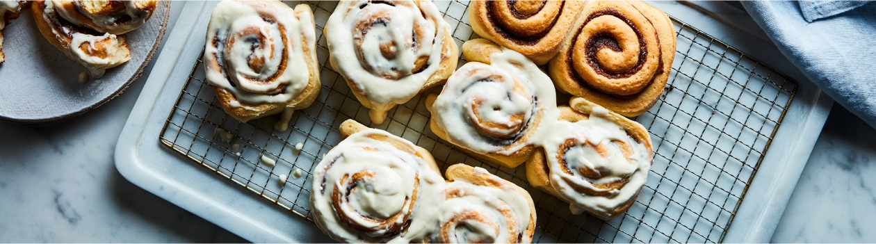 Marble surface with cooling rack of glazed cinnamon rolls, with side plate of half-eaten roll to the side