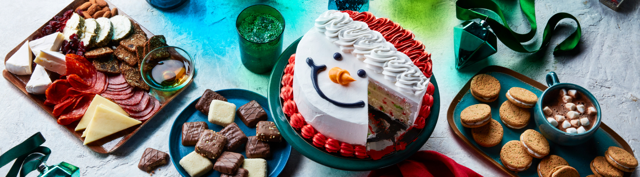 Light blue surface with plates and platters of charcuterie, cookies, ganache biscuits, and a whole snowman layer cake