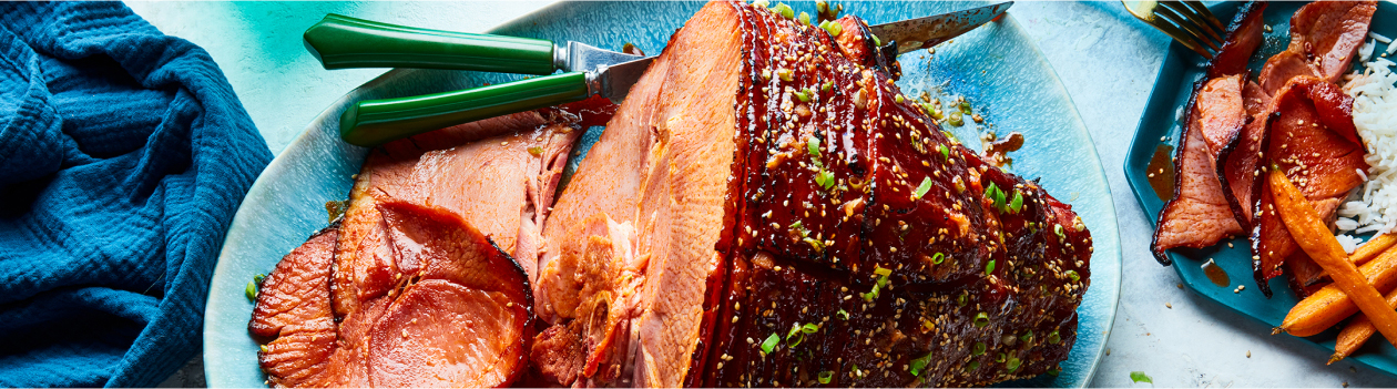 Oval light blue platter with Gochujang & Maple Glazed Spiral Ham with sesame seed and green onion garnish
