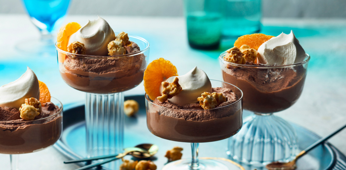 clear glass cups with chocolate mousse, whipped cream, clementine slice and caramel popcorn