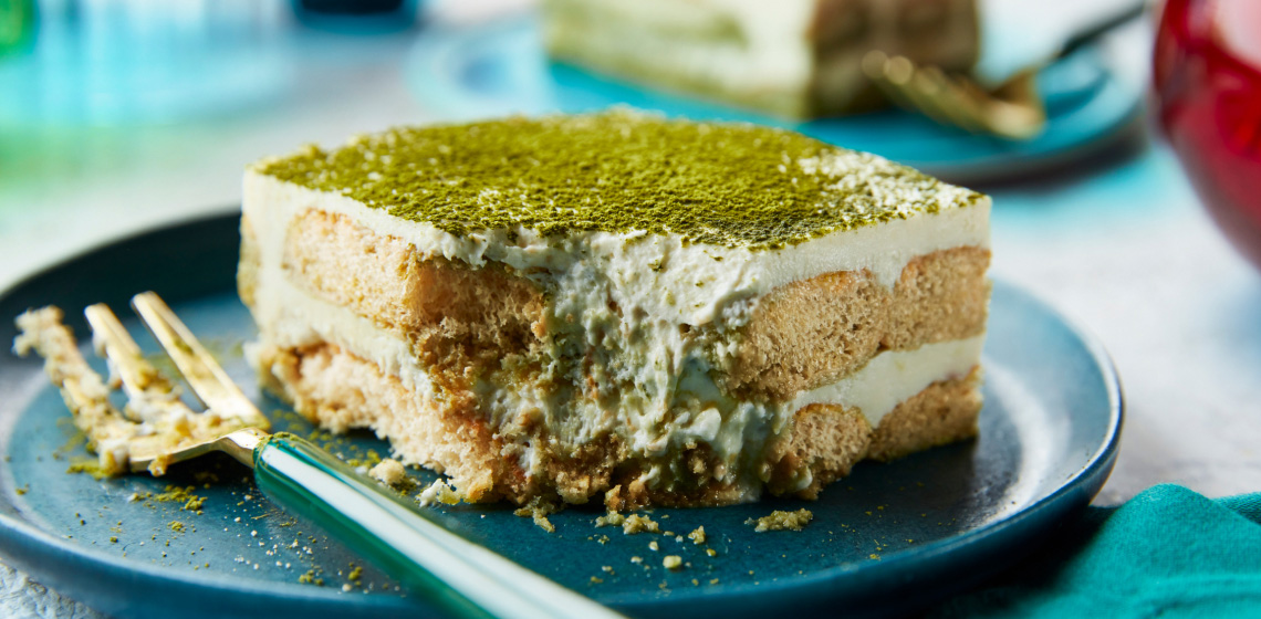 Blue side plate showing side profile of one square serving of matcha white chocolate tiramisu with a bite taken out of the front left corner