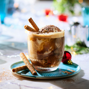 An easy holiday cocktail in a lowball glass—espresso, ice cream, rum, and cola—on a white marble surface with Christmas decorations.