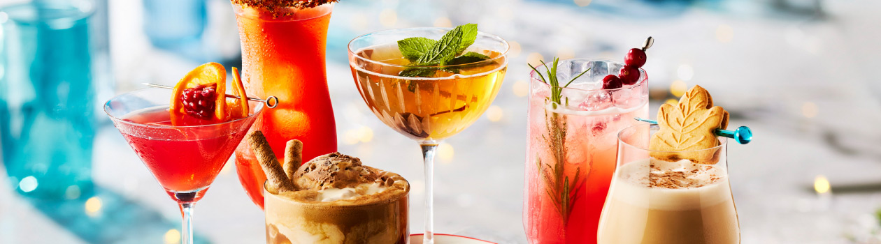 A white marble table with six retro holiday cocktails arranged with holiday decorations.