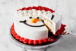 Confetti cake decorated as a snowman’s face with one slice cut and being removed from the cake.