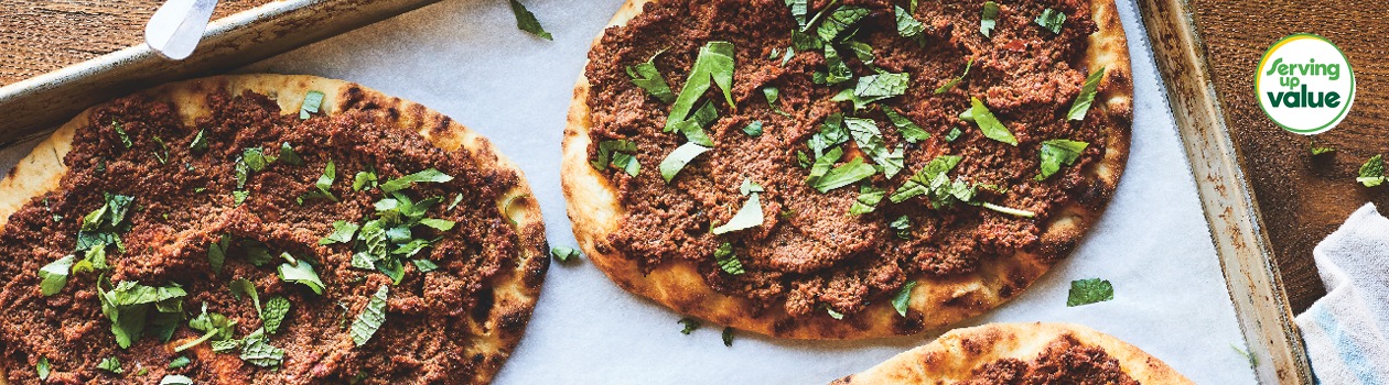 Baking sheet with four meat-topped flatbreads garnished with fresh mint and parsley