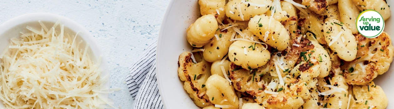 Large white serving bowl filled with gnocchi and roasted cauliflower on marble tabletop
