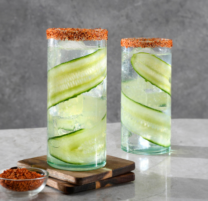 Two glasses rimmed with spice featuring Betty Buzz Meyer Lemon Club Soda and tequila lined with cucumber ribbon and placed next to each other.