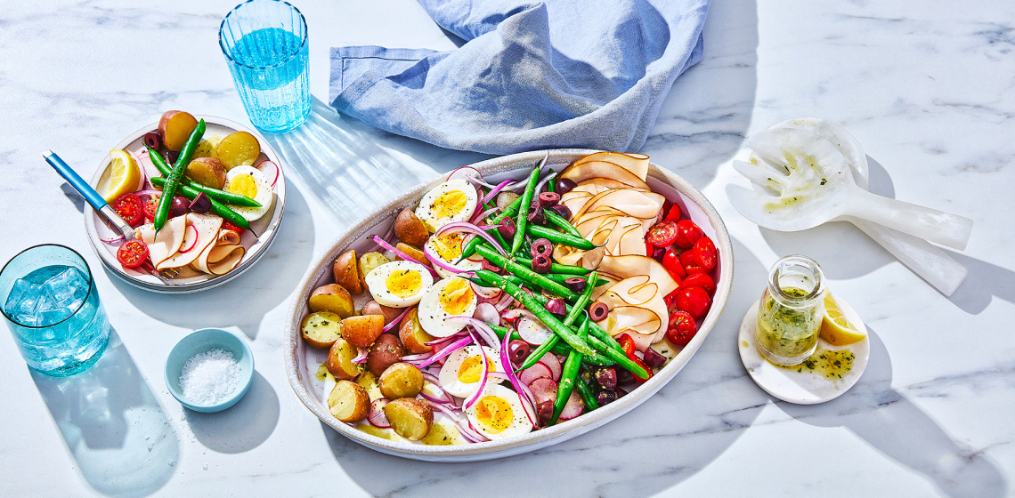serving platter of classic nicoise salad with potato, beans, hard-boiled egg, deli meat and tomatoes