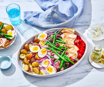 serving platter of classic nicoise salad with potato, beans, hard-boiled egg, deli meat and tomatoes