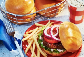 Dressed burger with basket of brioche burger buns in background.