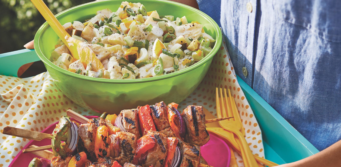 serving tray with green bowl of dill pickle potato salad and a plate of grilled kabobs