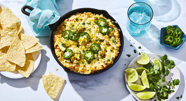 cast-iron pan of Mexican-inspired Street Corn Party Dip with tortilla chips on the side