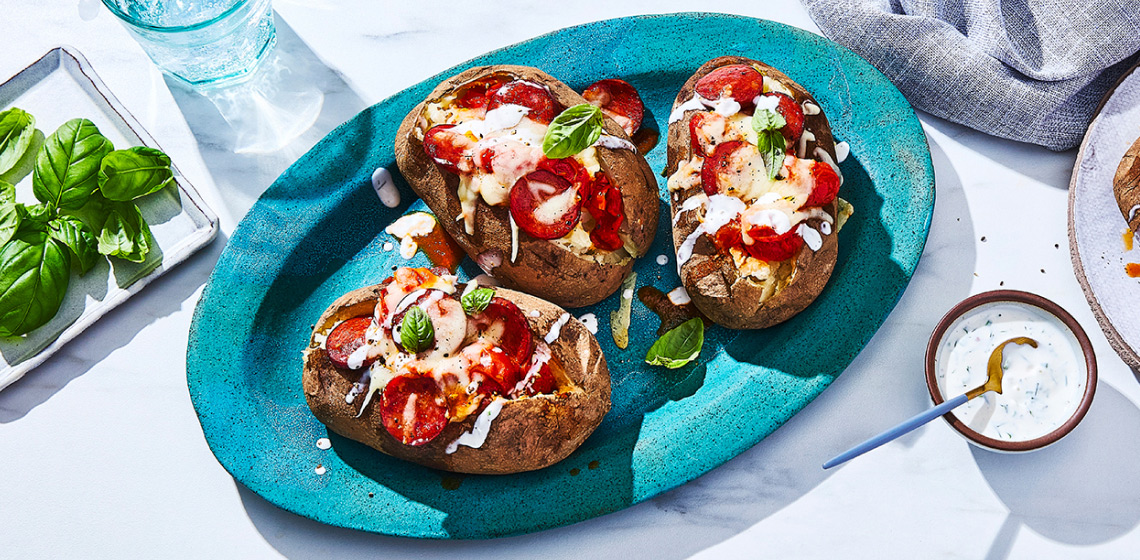 Serving platter and side plate with pepperoni and cheese topped baked potatoes with a ranch drizzle