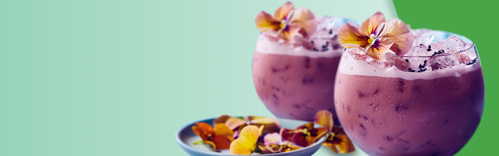 Low rounded glass of purple iced cocktail with edible floral garnish