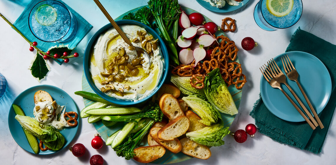 Overhead shot of dirty martini dip with baguette, vegetables, and pretzels