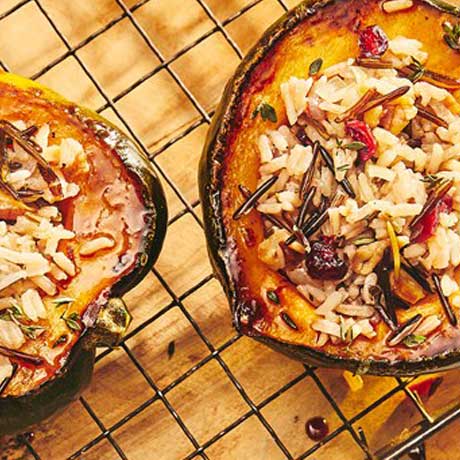 Two acorn squash halves filled with a wild rice stuffing sitting on a cooling rack over a wooden cutting board.