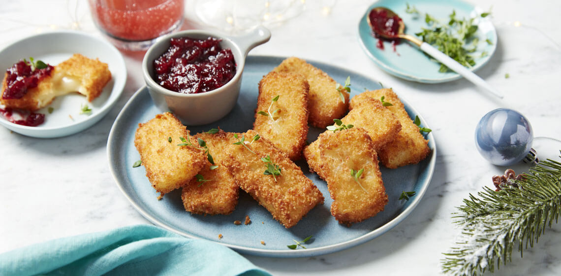 Breadcrumb coated brie fingers on a blue plate next a bowl of a cranberry and port topper.