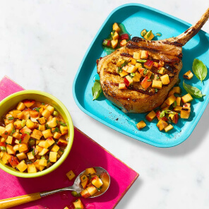 Turquoise coloured plate with a grilled Nagano Hotel Cut Pork Chop, topped with a grilled peach salsa and a pink bowl with the salsa by the plate.