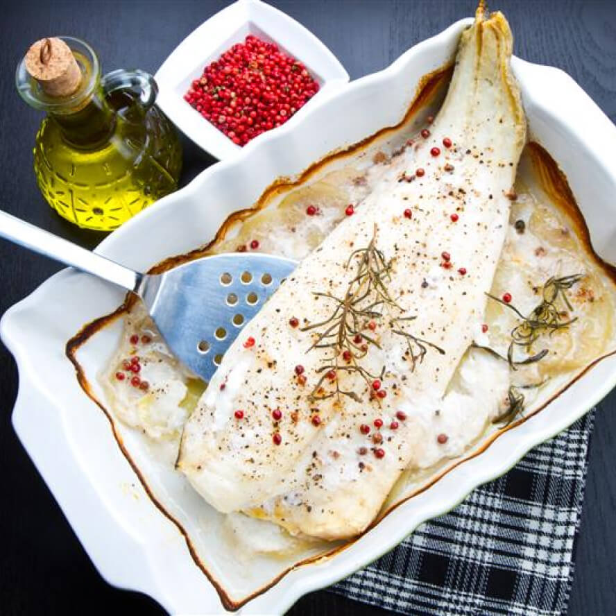Baked pickerel being lifted out of casserole dish
