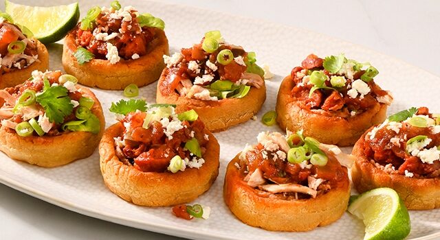 Plate of Mexican-style sopes topped with cilantro, refried beans and rotisserie chicken.