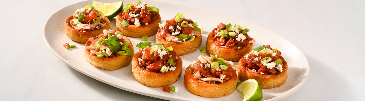 Plate of Mexican-style sopes topped with cilantro, refried beans and rotisserie chicken.