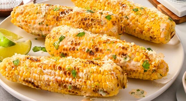 Plate of Mexican-style street corn with bowls of cheese and cilantro to the side
