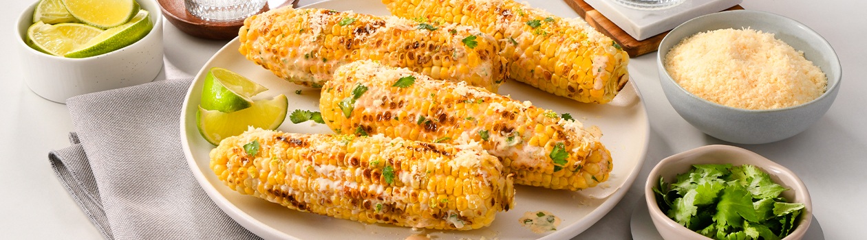 Plate of Mexican-style street corn with bowls of cheese and cilantro to the side