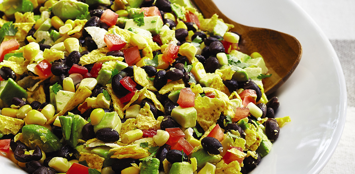 A plate of bean & corn taco salad on a red and white striped tablecloth