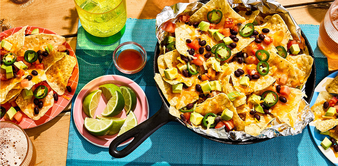 Overhead shot of campfire nachos in a skillet, topped with jalapenos, black beans, cheese, and avocado.