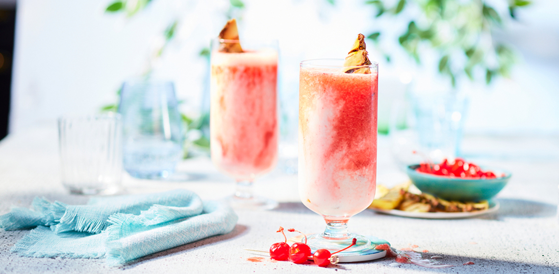 Tall glasses full of an icy Cherry Miami Vice Cocktail on a gray countertop with turquoise napkins off to the side.