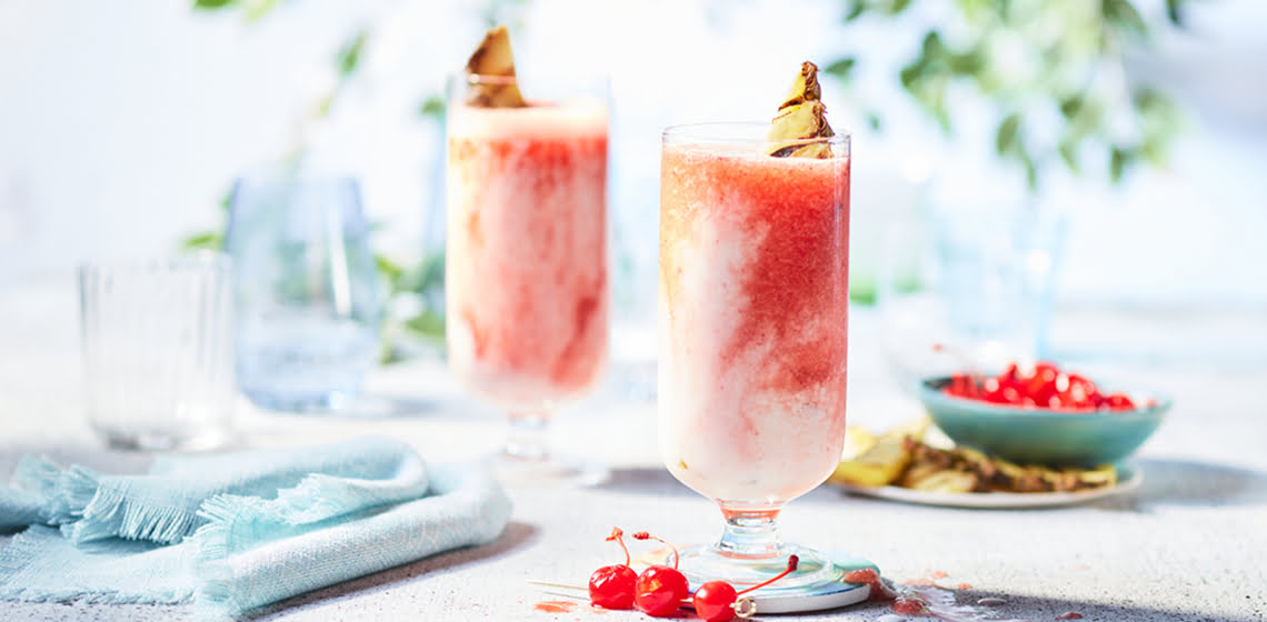 Tall glasses full of an icy Cherry Miami Vice Cocktail on a gray countertop with turquoise napkins off to the side.