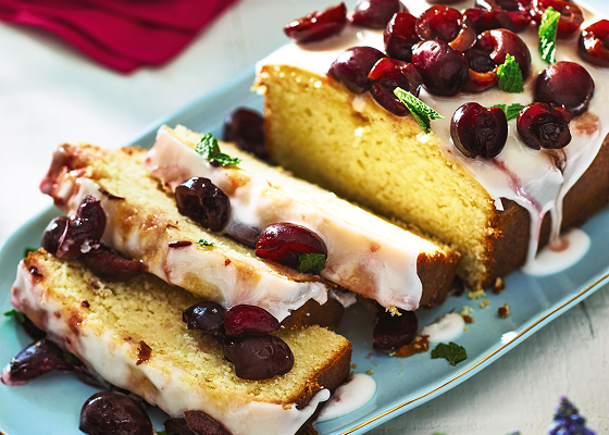 Sliced glazed lemon half-pound cake with cherries on a blue plate.