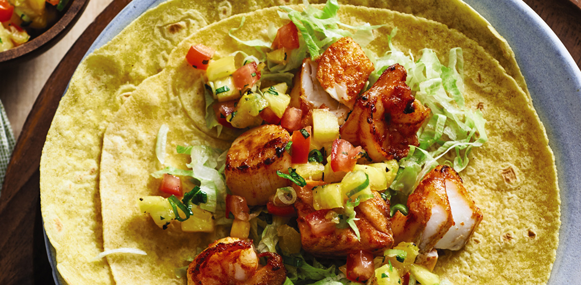 Yellow tortillas with a pile of crispy seafood and tarragon salsa in the middle all on a light blue plate with a spoon off to the side with more salsa.