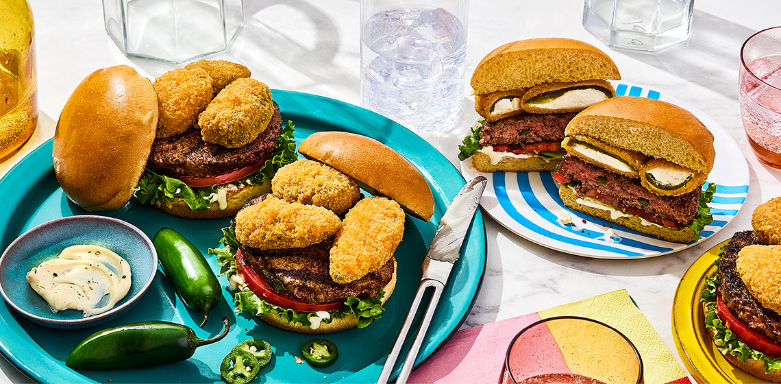 Jalapeno popper burgers topped with jalapeno poppers, burgers that are cut in half in the background