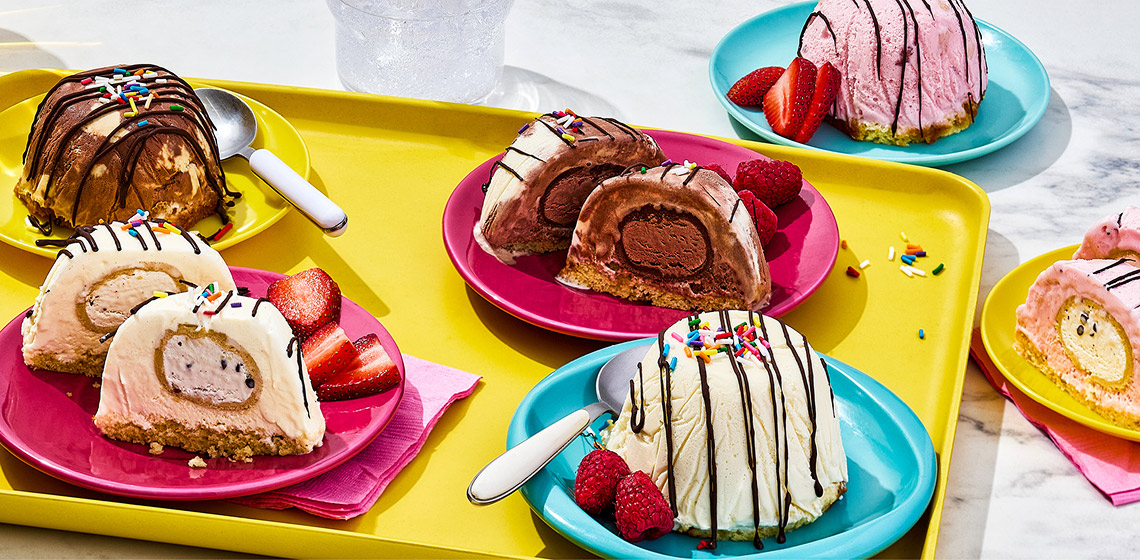Six plates with the Dough Chi Ice Cream Bombes with some cut open to see the Dough Chi Bites and on the side there are berries and spoons.