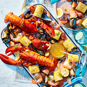 Platter filled with seafood boil of whole lobster, corn, mussels, shrimp, potatoes, and lemon.