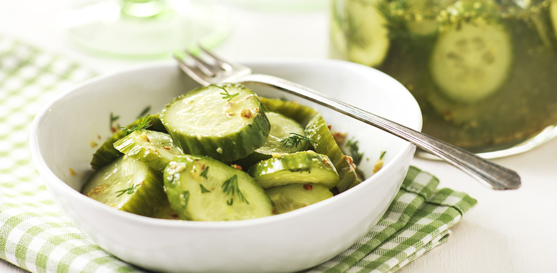 A bowl of Fresh Baby Dill Pickles with a fork lying on top and more pickles in a jar with the brine.