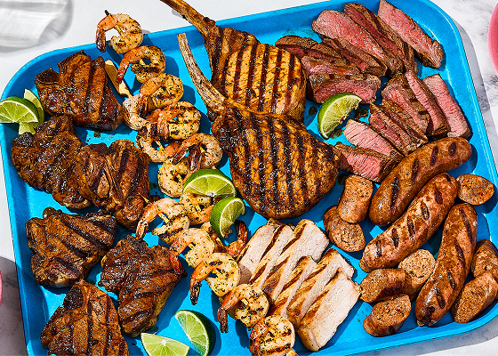 A large platter of all the Braai meats and seafood with a small plate of some off to the side, a small plate of grilled corn and two bowls with pasta and potatoes.