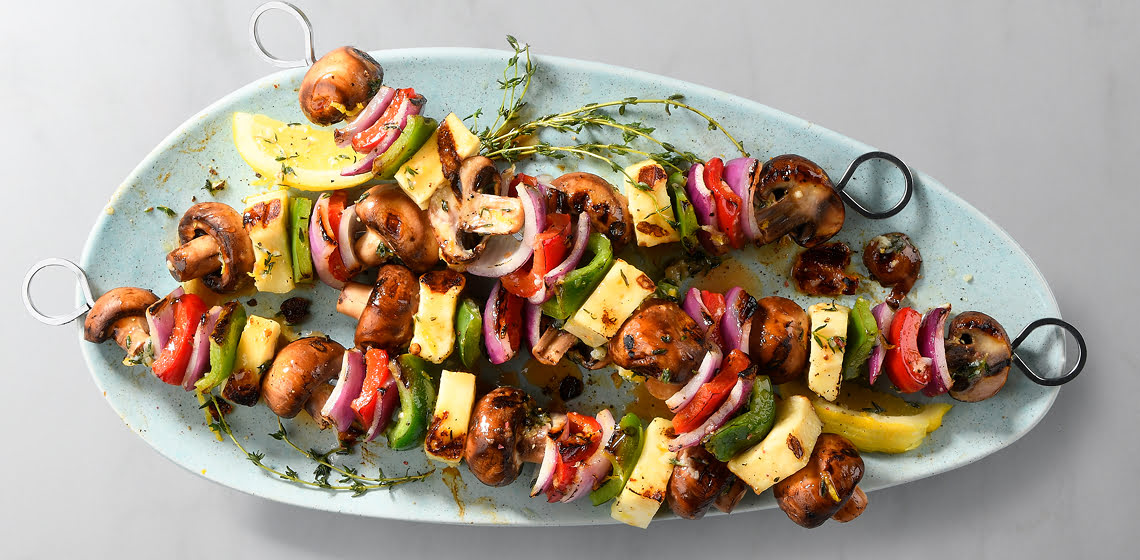 Four grilled cremini mushroom and halloumi cheese skewers on a blue plate.