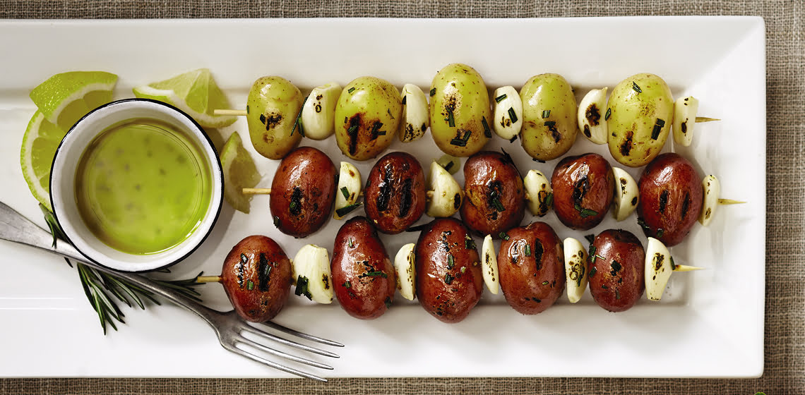 Three mini potato and garlic skewers on a white plate
