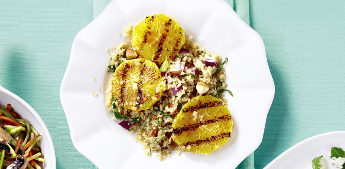 White scalloped plate with a grilled orange and quinoa almond salad inside.