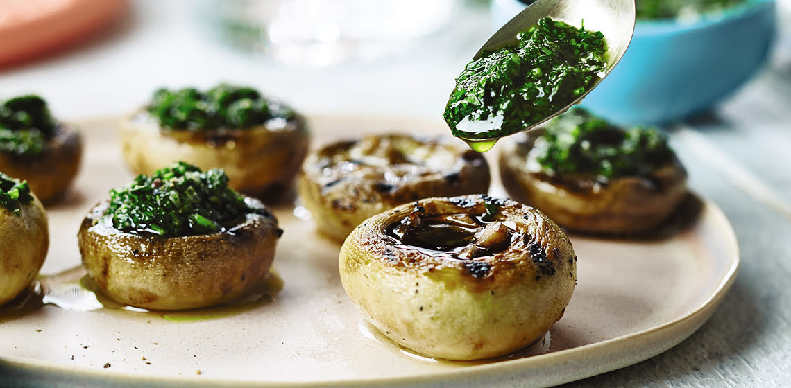 Seven grilled pesto-filled mushrooms on a white plate.