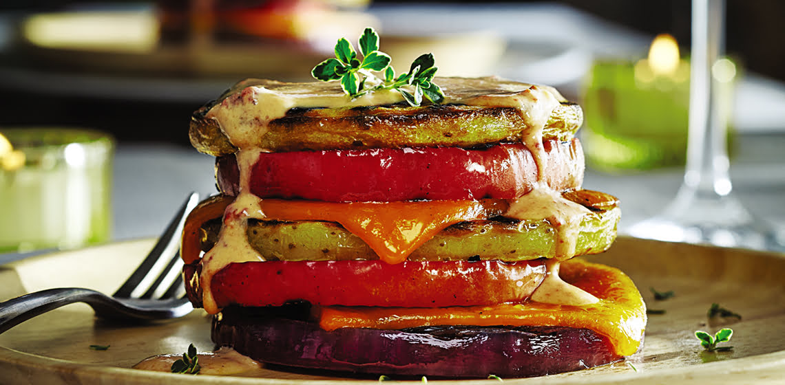 Grilled potato apple stack with chipotle sauce on a wooden plate with a glass of white wine in the background.