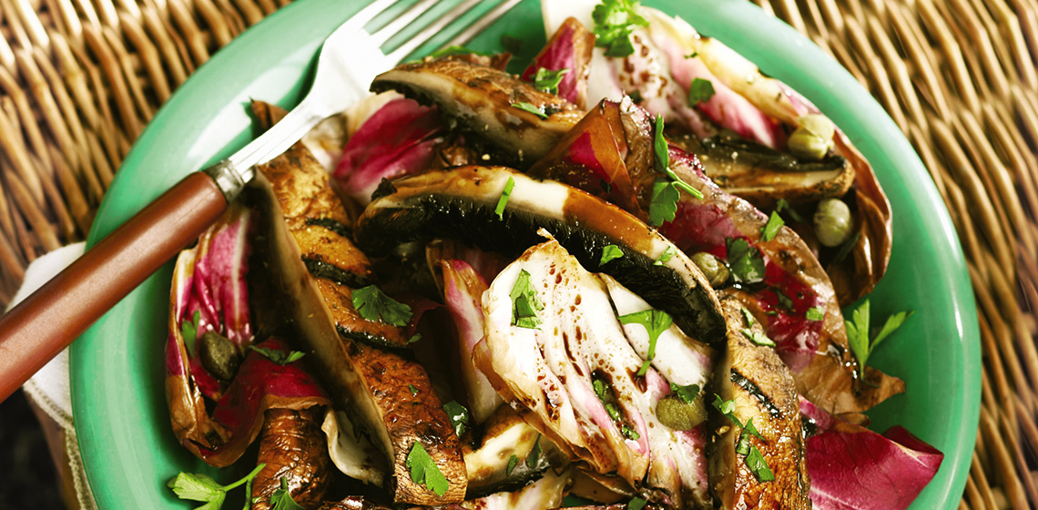 Grilled radicchio and portobello mushrooms on a green plate with a fork on top of a picnic basket.