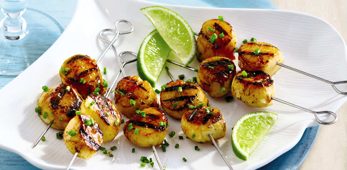 Metal skewers with Grilled Scallops with Mango Curry Glaze with wedges of lime and spring onion sprinkled on top.